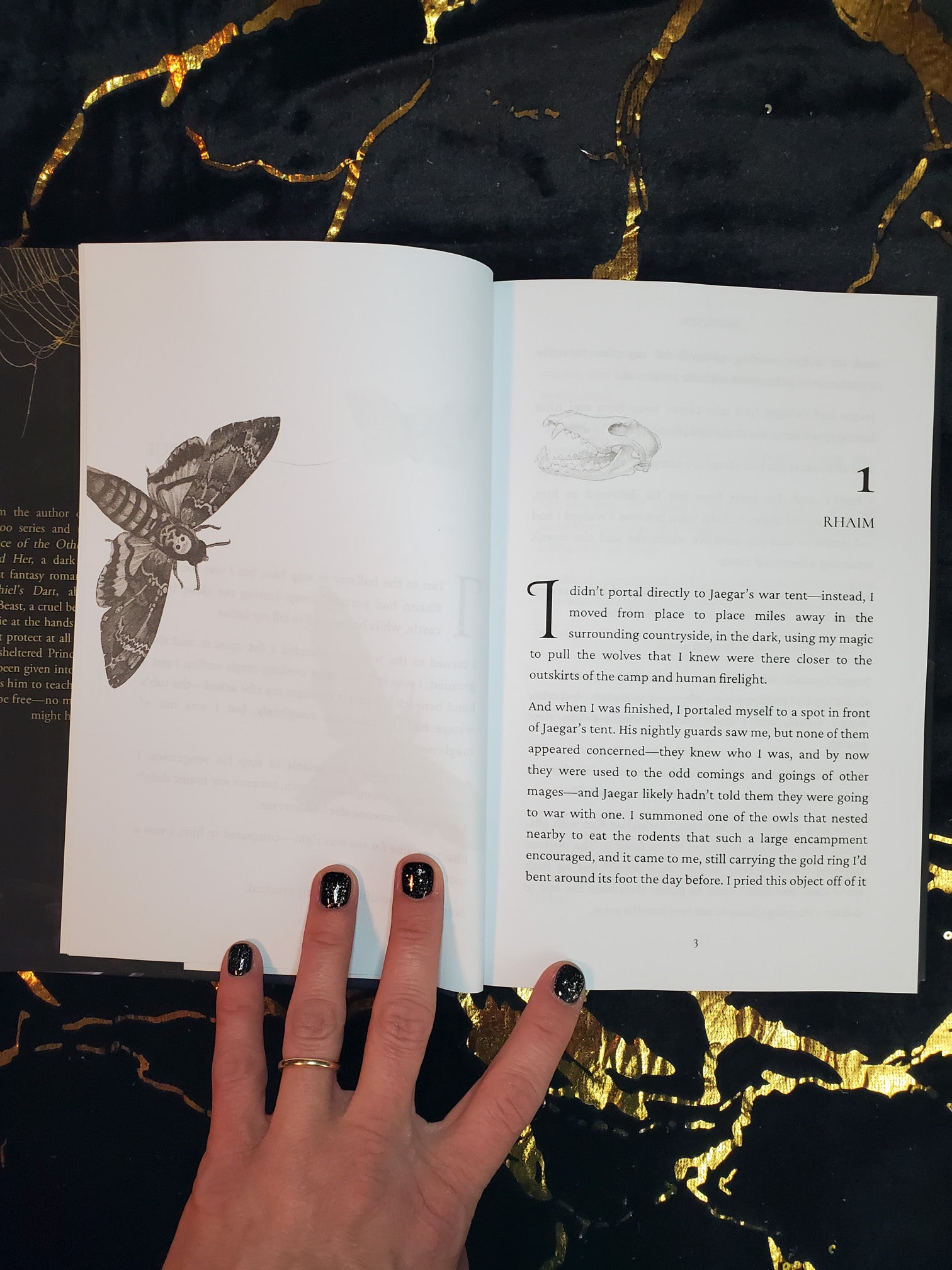 Photo of Chapter one spread for Break Her by Cassie Alexander. Left is a moth, right shows chapter one with an animal skull illustration. Book is sitting on a black and gold background.