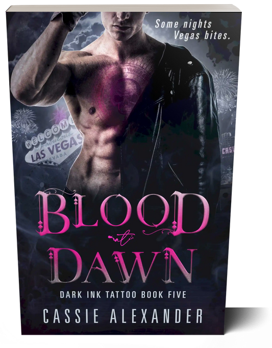 Cover for Blood at Dawn: Dark Ink Tattoo Book Five by Cassie Alexander. A man wearing a black leather jacket over one shoulder with a pink skull and circular tattoo on his chest stands in front of a Las Vegas skyline. Tagline reads: Some nights Vegas bites. Shown as a paperback book.